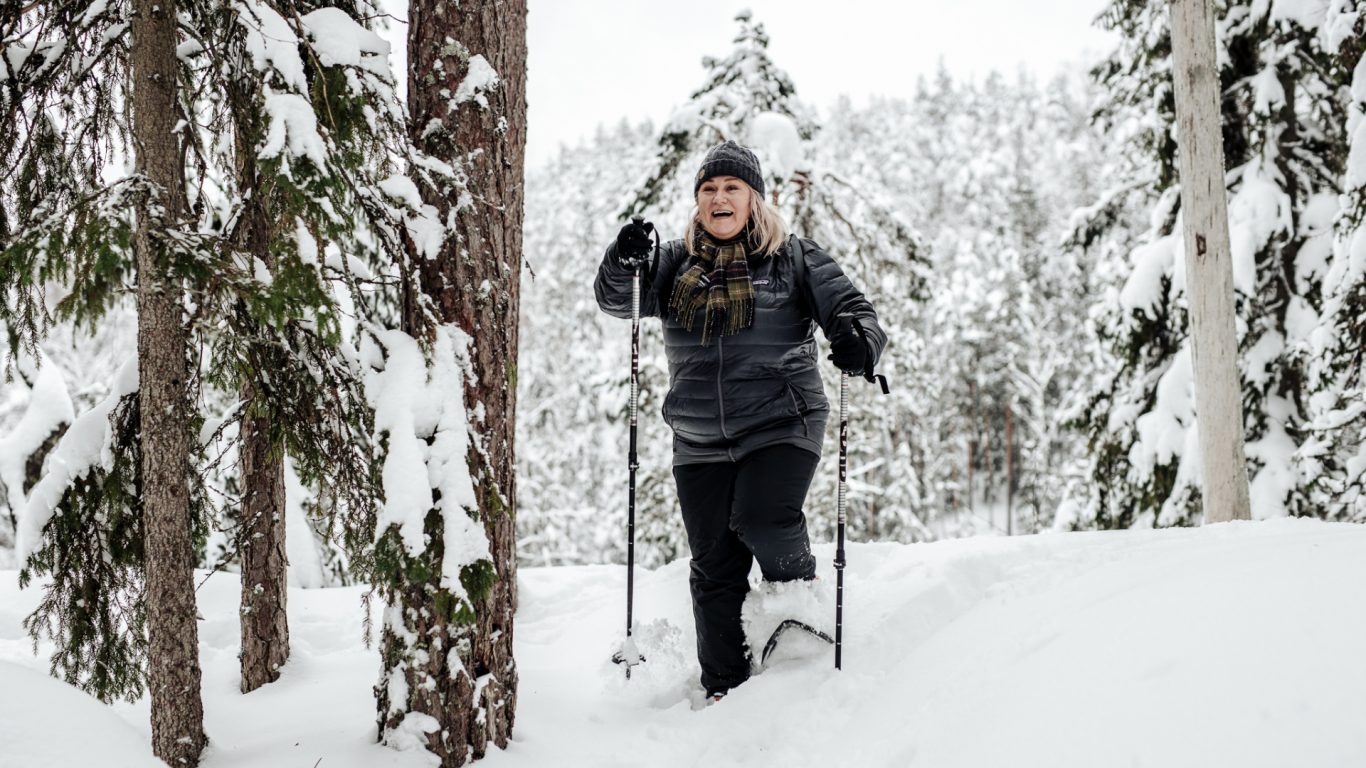 Iloinen nainen lumikenkäilemässä talvisessa luonnossa