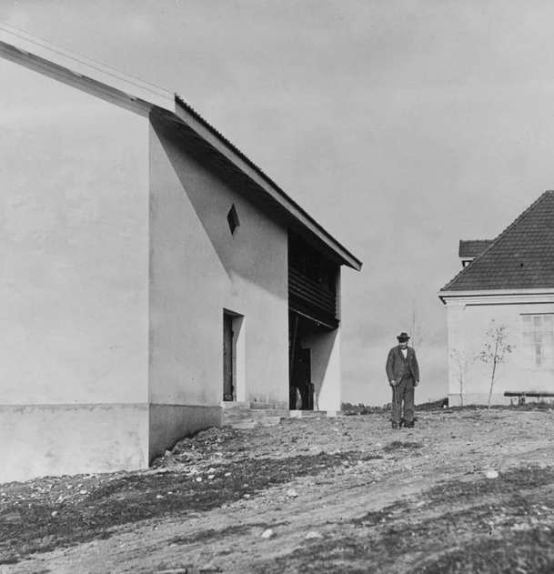 Vanha mustavalkoinen valokuva, jossa mies seisoo kivisten rakennusten välissä keväisessä säässä.