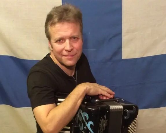 Pepe Niilahti nojaa harmonikkaan Suomen lipun edessä