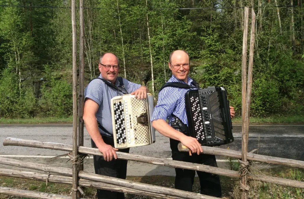 Seppo Soittila ja Seppo Lankinen harmonikat kädessä nojaavat aitaan metsän edustalla