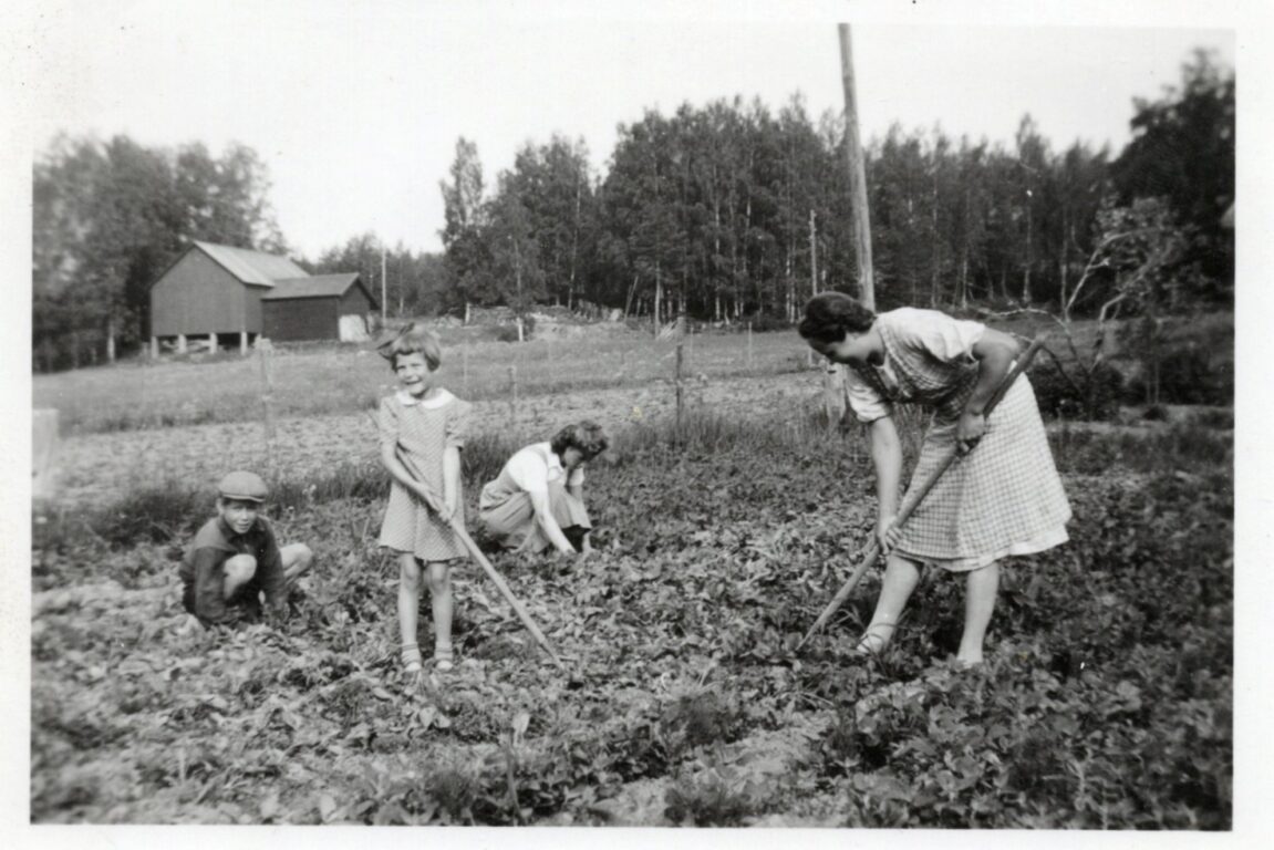 Mustavalkoinen kuva naisista ja lapsista peltotöissä