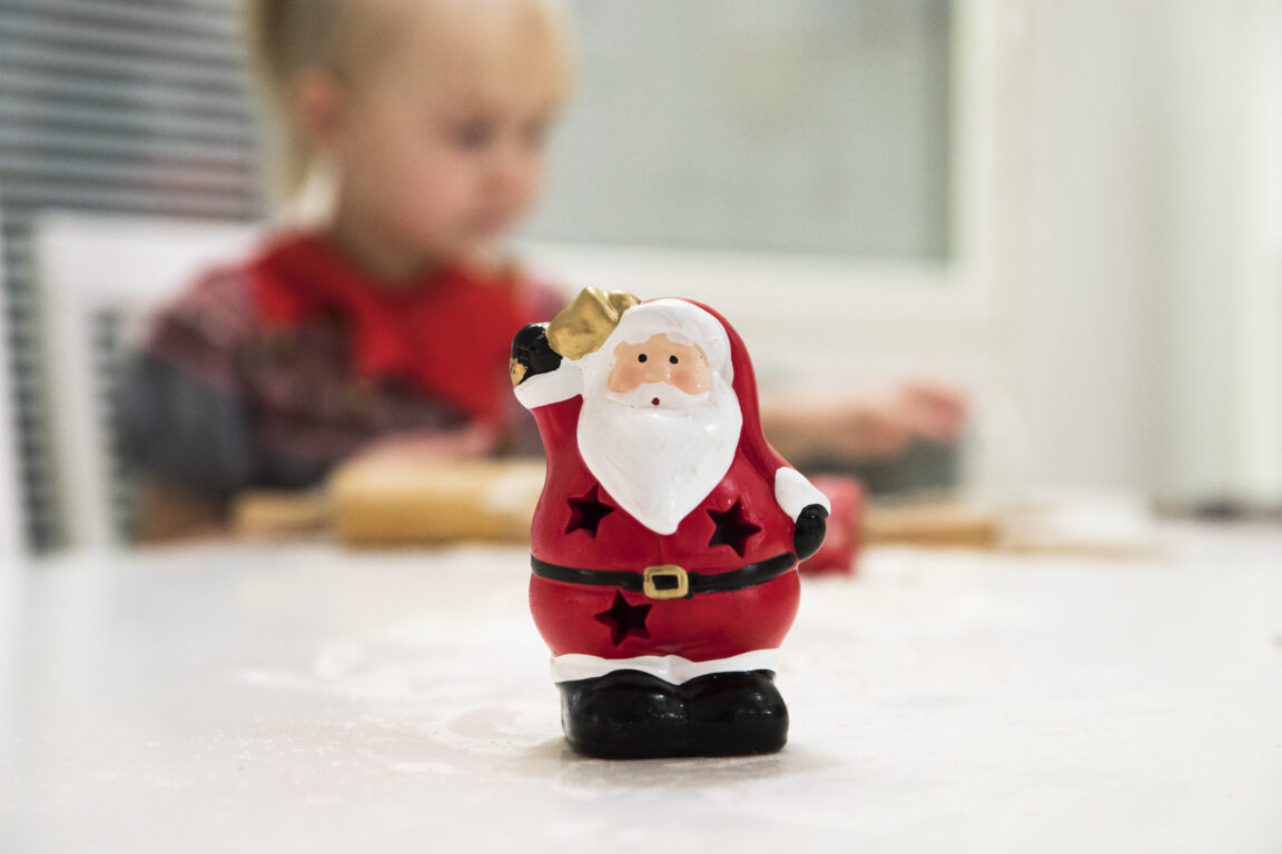 Etualalla joulupukkikoriste, takana näkyy sumeana tyttö punaisessa paidassa.