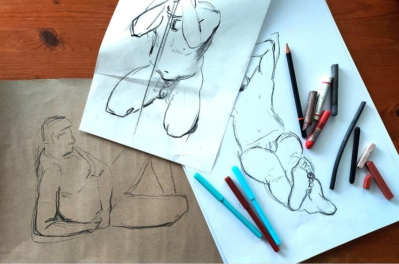 Elävän mallin piirustuksia ja kyniä pöydällä.