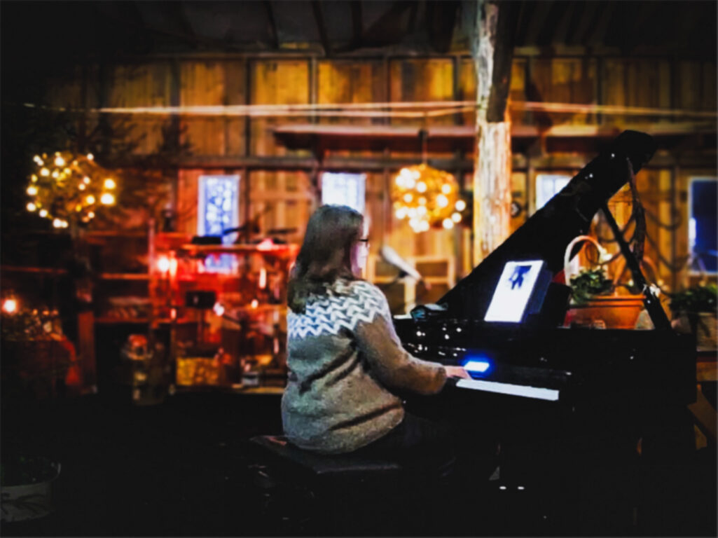 Nainen soittaa pianoa jouluisessa tilassa.