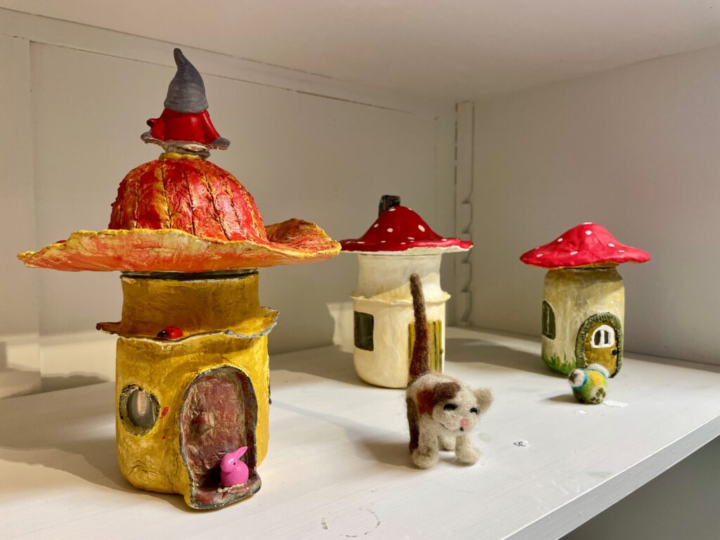 Kuvassa on käsityönä massasta tehtyjä sieniä, jotka on muotoiltu pieniksi kodeiksi. Sienten edessä on pieniä eläinhahmoja.
