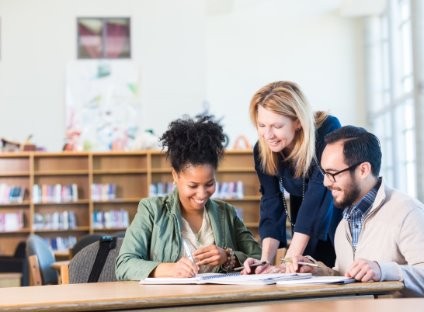 Kolme henkilöä tutkivat papereita, kaikki hymyilevät.