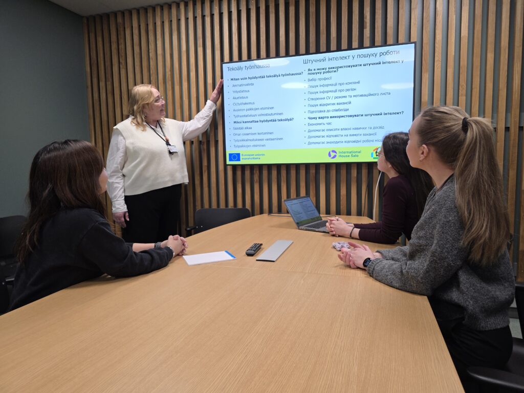 Työpajassa kolme osallistujaa seuraa näytöltä esitettävää materiaalia.