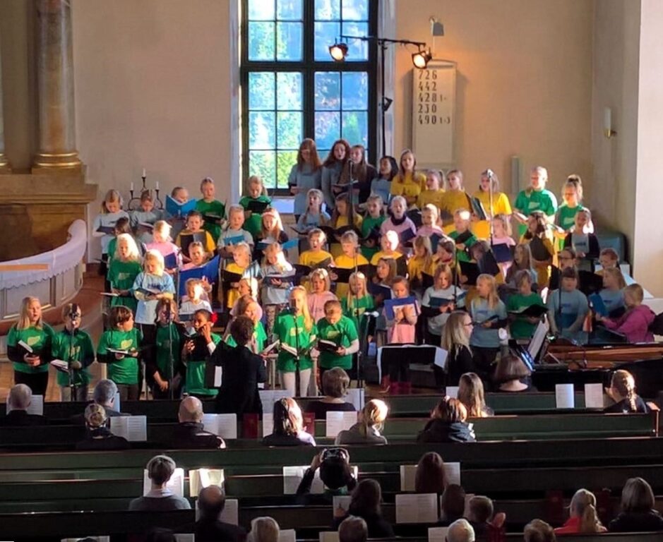 Suuri määrä lapsikuorolaisia värikkäissä paidoissaan Uskelan kirkossa