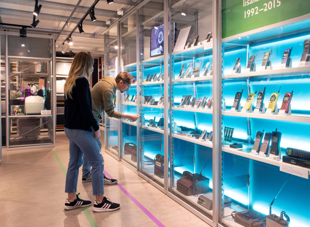 Museoasiakkaat kännykkävitriinin esineitä katselemassa.