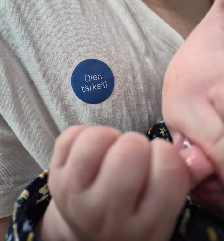 Vauva äitinsä sylissä, paitaan liimattu MLL:n tarra 